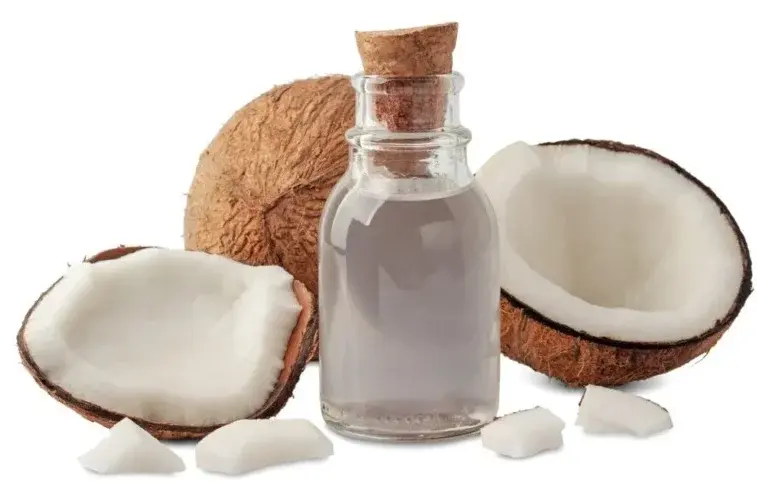 روغن نارگیل در ظرف شیشه‌ای با قاشق چوبی و دانه‌های نارگیل اطراف آن