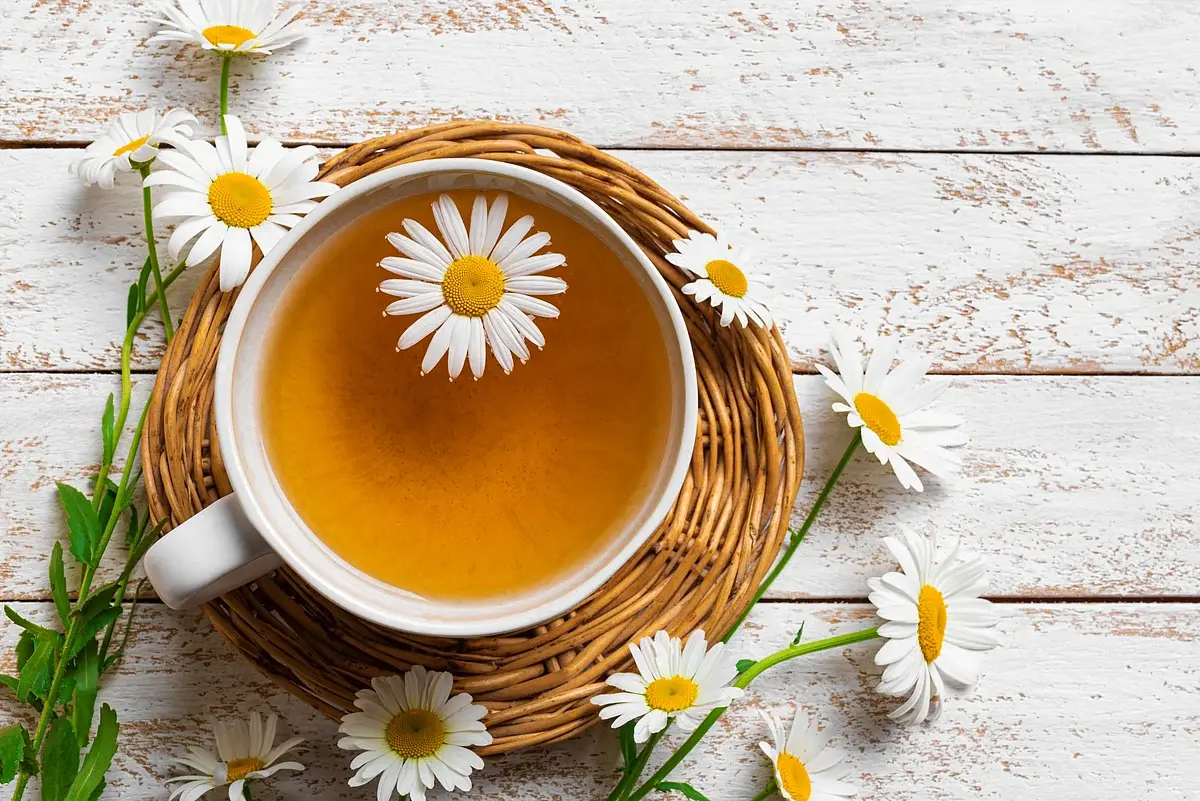 چای گل گاوزبان در فنجان سفالی با گل‌های تازه در پس‌زمینه